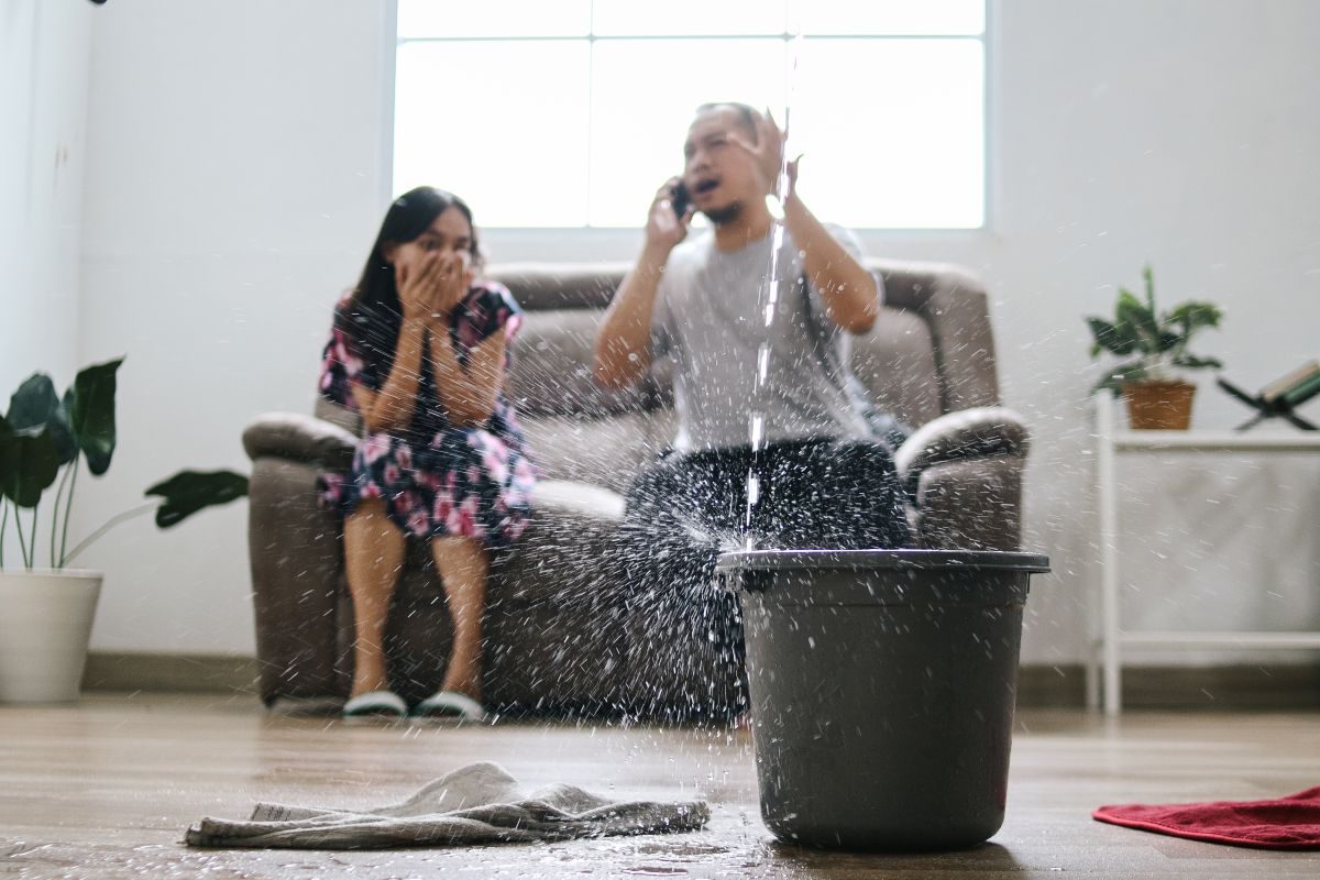 Rainwater pouring through a ceiling leak into a bucket in a living room